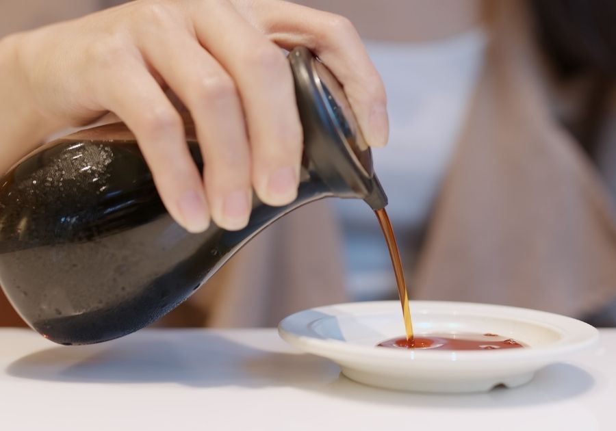 Hand Holding Bottle Pouring Soy Sauce on Plate
